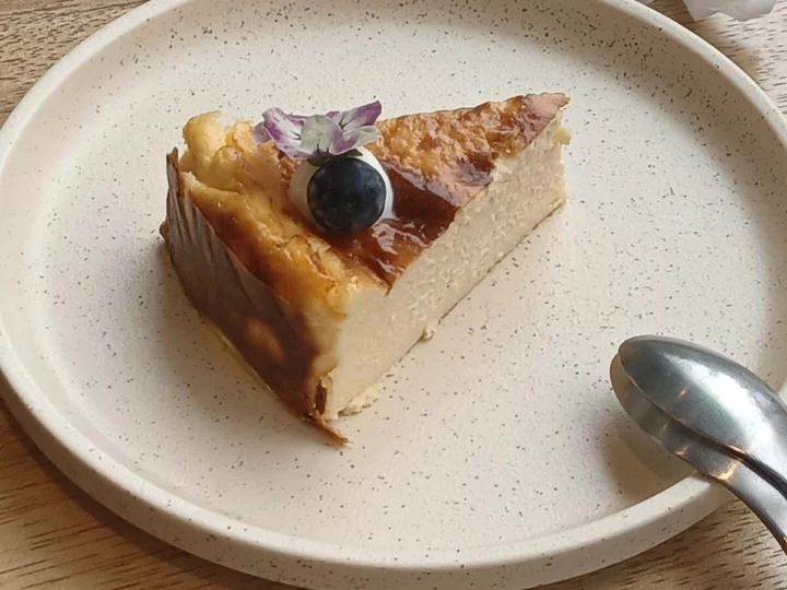 A slice of burnt cheesecake with a blueberry on a pale plate