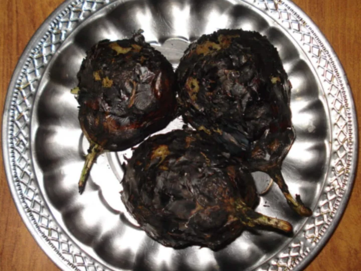 Whole charred aubergines on a metal platter