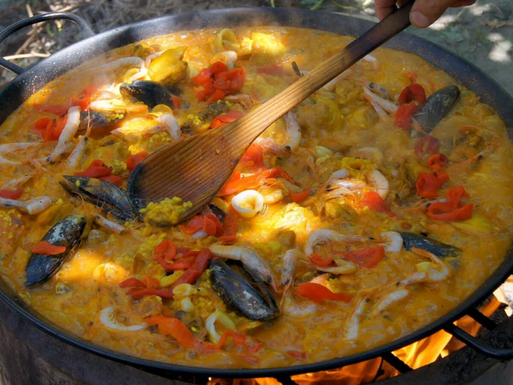 A seafood paella cooking in a pan over a wood fire