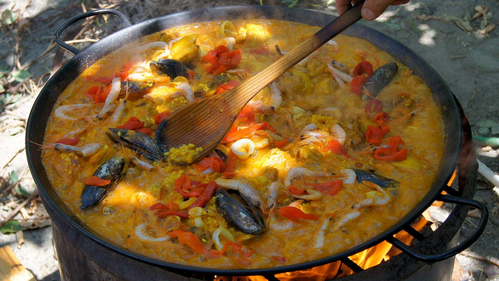 A seafood paella cooking in a pan over a wood fire
