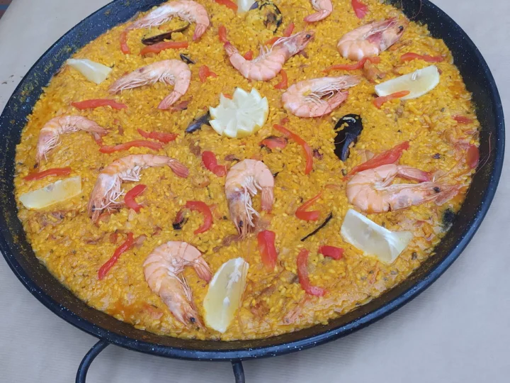 A paella with prawns and lemon wedges in a wide pan