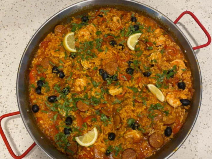 A paella in a steel pan with lemon slices, seen from above