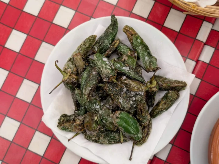 Blistered green peppers on a white plate over a checked cloth