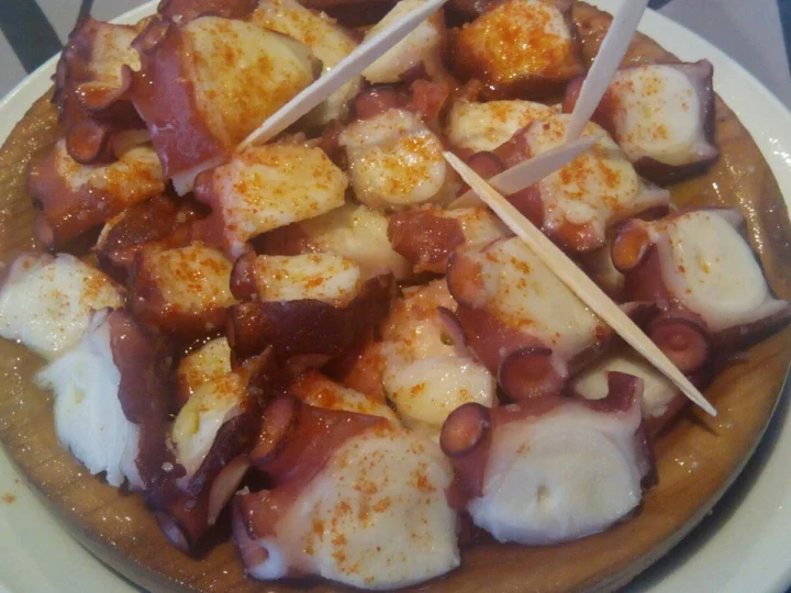 Sliced octopus on potatoes with paprika, on a wooden plate