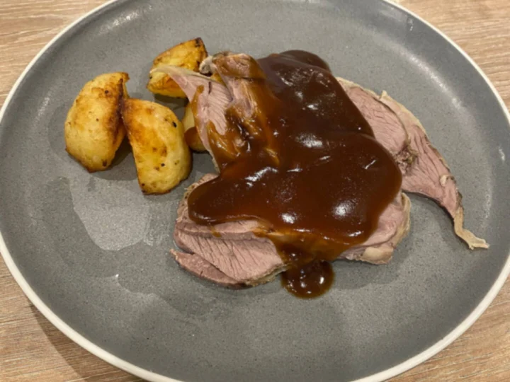 Roast lamb with gravy and potatoes on a grey plate
