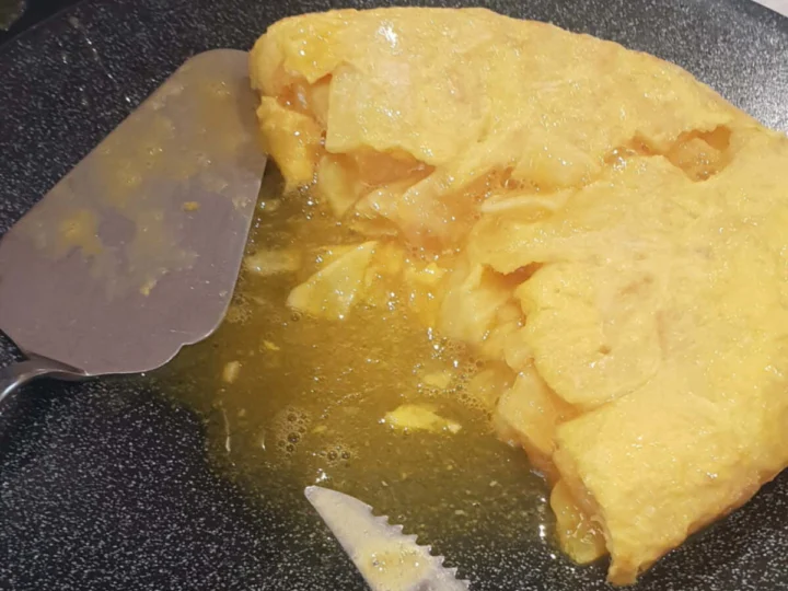 A thick potato omelette on a dark plate with a knife